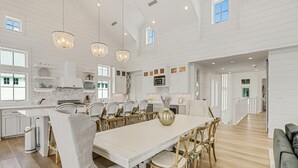A spacious kitchen with white cabinetry, a dining area with a large table and chairs, and a view of the living area. - Lakeside Home@Cinnamon Shore South w/ Gourmet Kitchen+On-Site Amenities (Port Aransas)