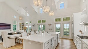 A spacious kitchen with a large island, white cabinetry, and a view of the outdoors through multiple windows. - Lakeside Home@Cinnamon Shore South w/ Gourmet Kitchen+On-Site Amenities (Port Aransas)