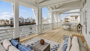 A covered outdoor deck with wooden flooring, white railings, and a view of houses along a waterway. - Lakeside Home@Cinnamon Shore South w/ Gourmet Kitchen+On-Site Amenities (Port Aransas)