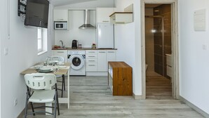 Una cocina funcional con lavadora, microondas y refrigerador. Incluye un banco de madera y una mesa con sillas.