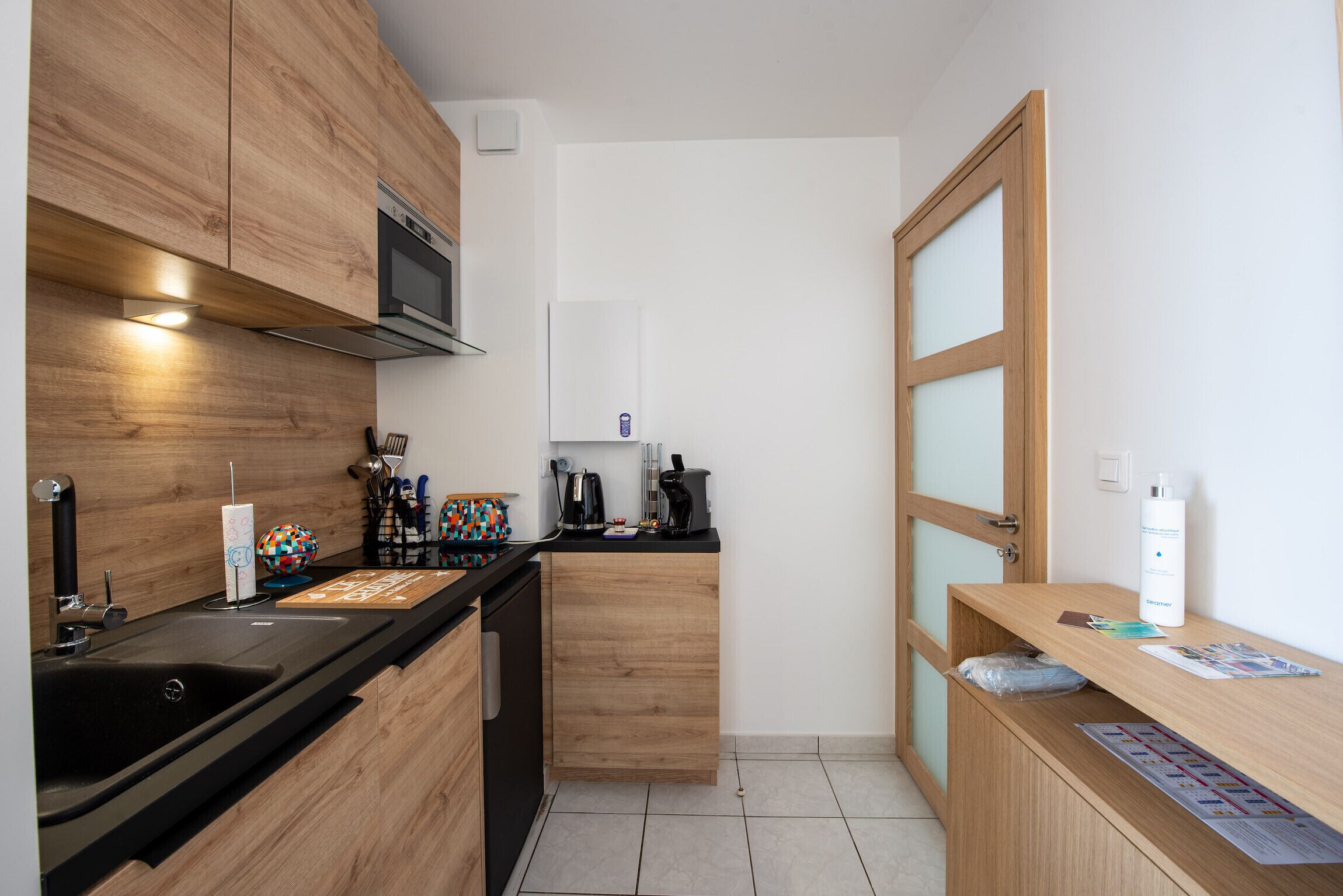 Une cuisine compacte avec des meubles en bois, un plan de travail noir et un four à micro-ondes encastré.