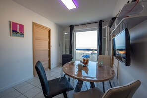 A dining area with a round table, chairs, and a view of the sea through a large window.
