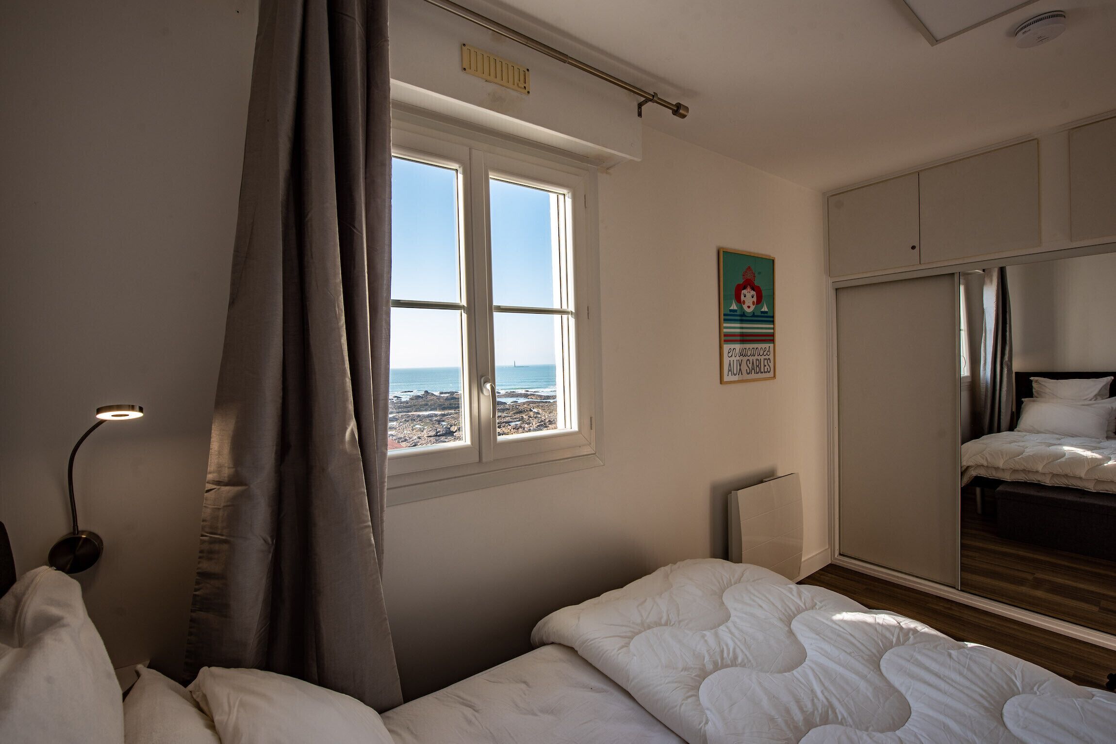 Een slaapkamer met een groot raam, een bed, een kledingkast en een bedlampje.