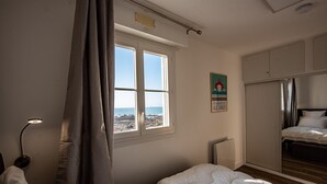 A bedroom with a large window, a bed, a wardrobe, and a bedside lamp.
