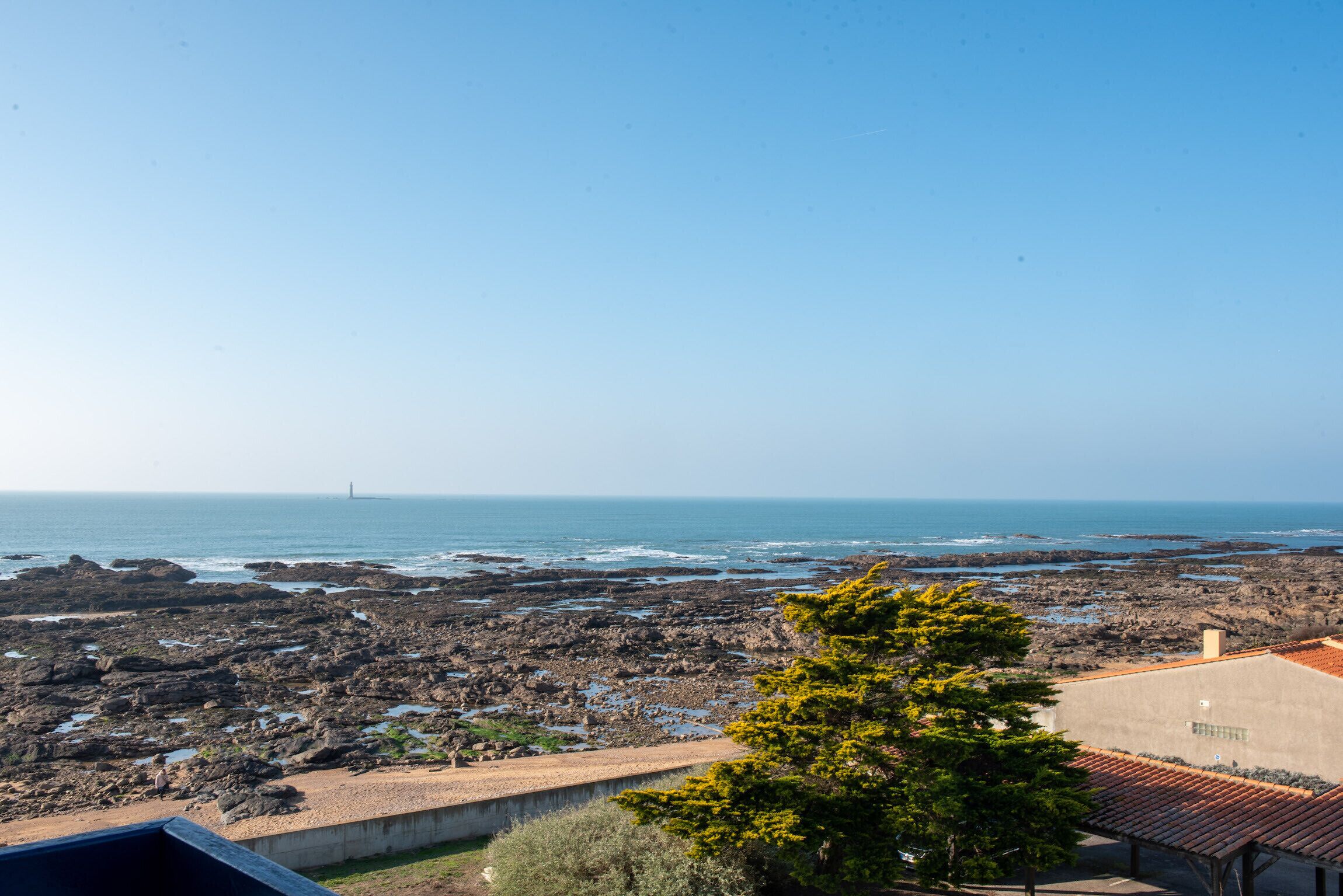 A coastal view with rocky terrain, a clear sky, and a distant lighthouse.