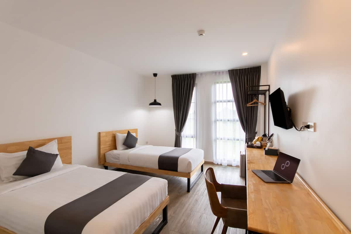 A hotel room with two beds, a desk with a laptop, a chair, and a TV mounted on the wall.