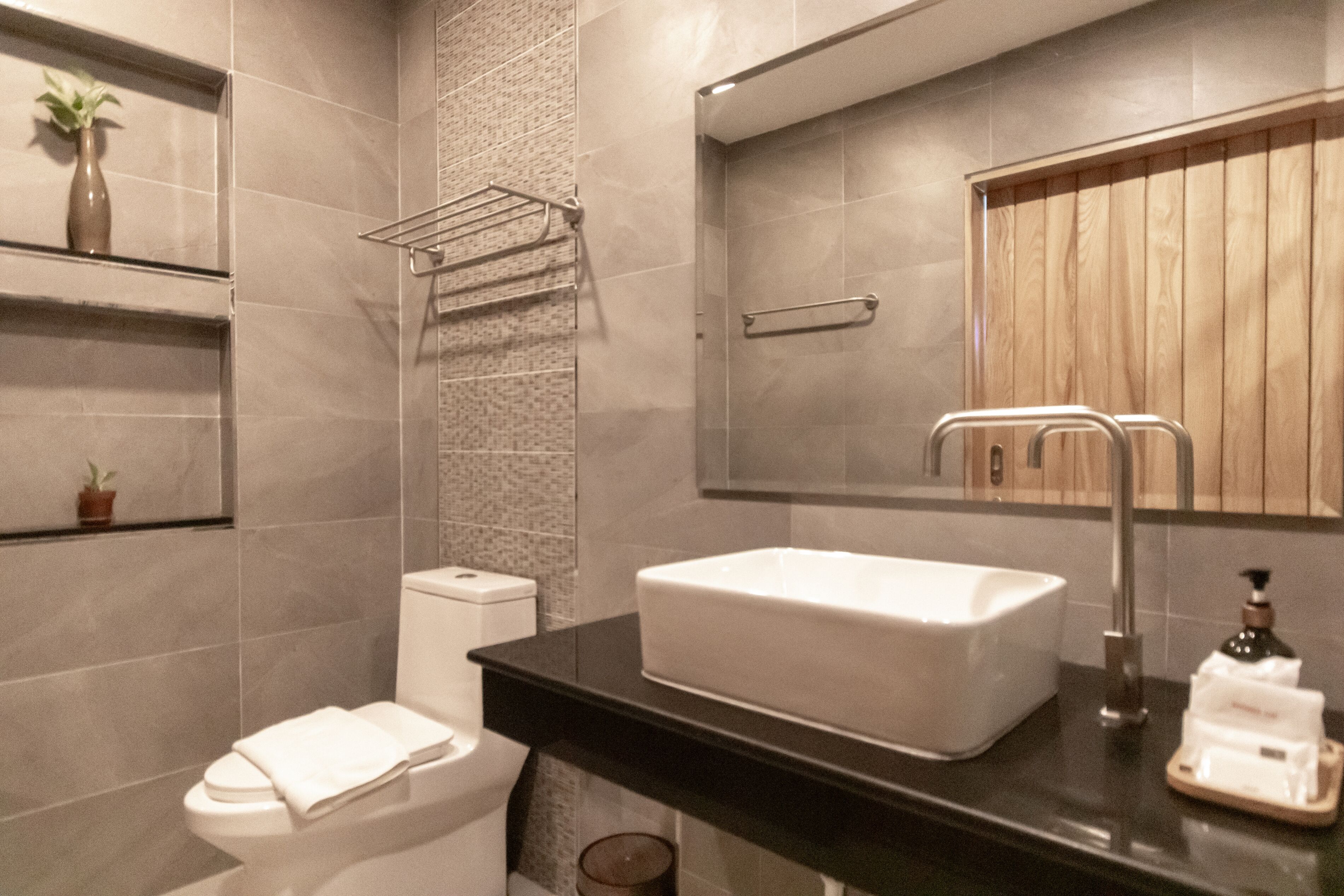 A modern bathroom with a white sink, black countertop, and a wooden vanity.
