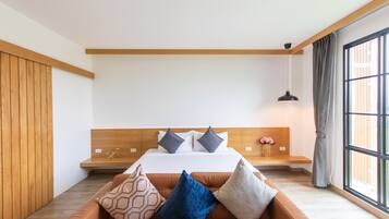 Un dormitorio moderno con cabecera de madera, una cama grande con muchas almohadas, un banco al pie de la cama y un ventanal con cortinas.