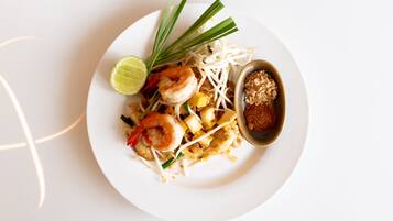 A plate of Pad Thai with shrimp, bean sprouts, lime, and a small bowl of sauce.