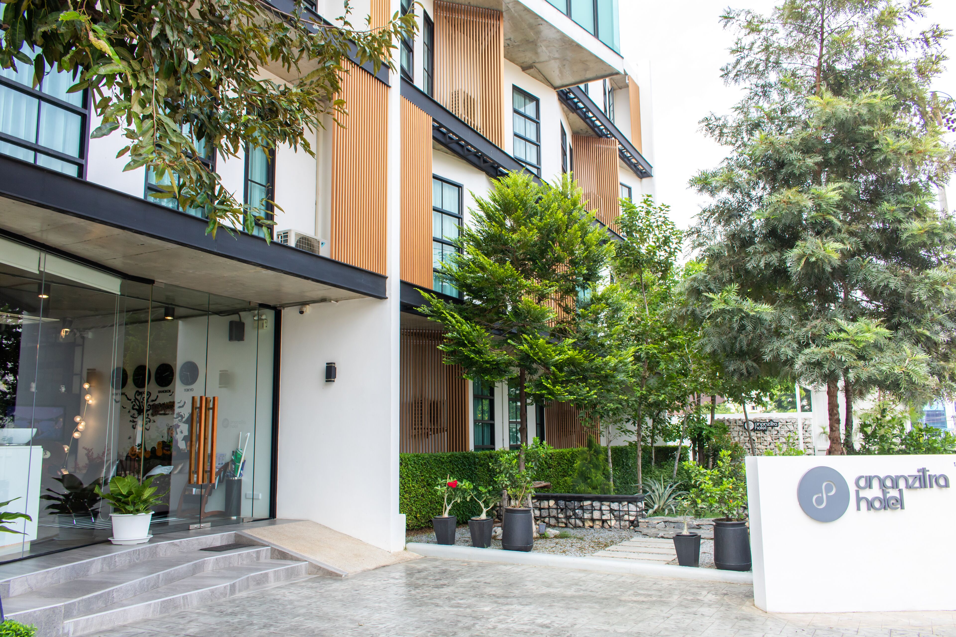 A modern hotel entrance with a glass facade, outdoor seating area, and potted plants.