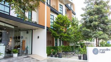 A modern hotel entrance with a glass facade, outdoor seating area, and potted plants.