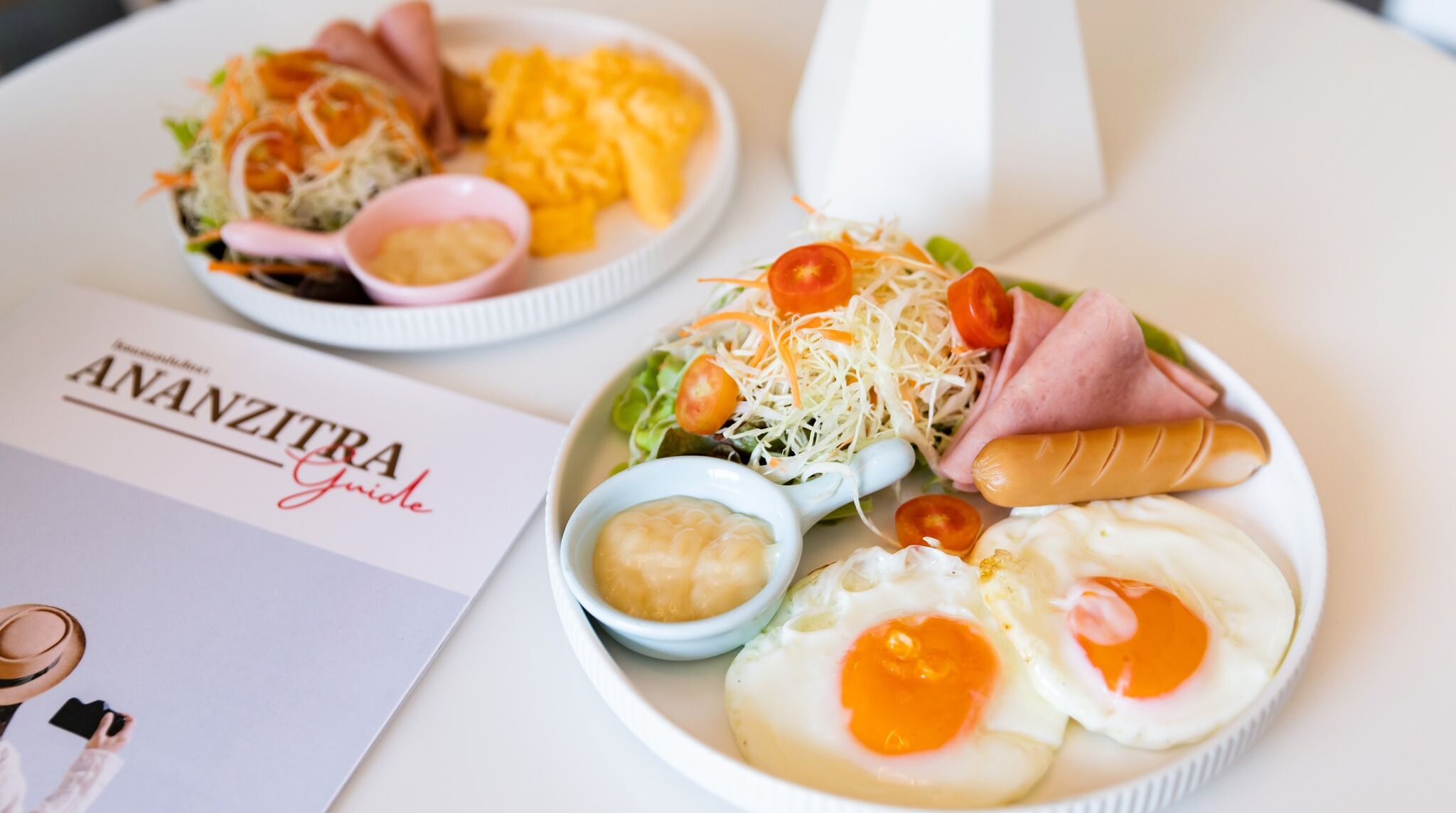 A table with two plates of food, a menu titled "ANANZITRA Guide", and a pair of sunglasses.