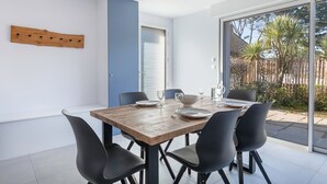 Zona pranzo moderna con tavolo in legno apparecchiato per quattro persone, sedie nere e vista del giardino esterno attraverso ampie vetrate.
