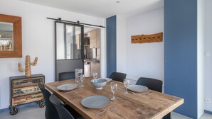 Zona pranzo con tavolo di legno apparecchiato per quattro persone, cucina sullo sfondo e parete decorata in blu.