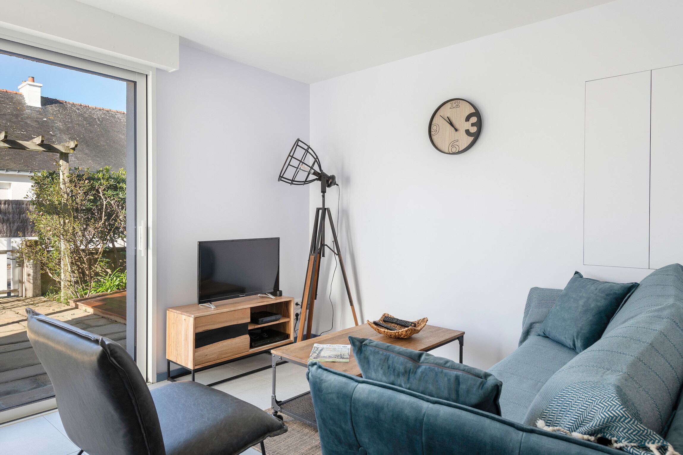A modern living room with a sofa, a TV, a lamp, and a clock on the wall.