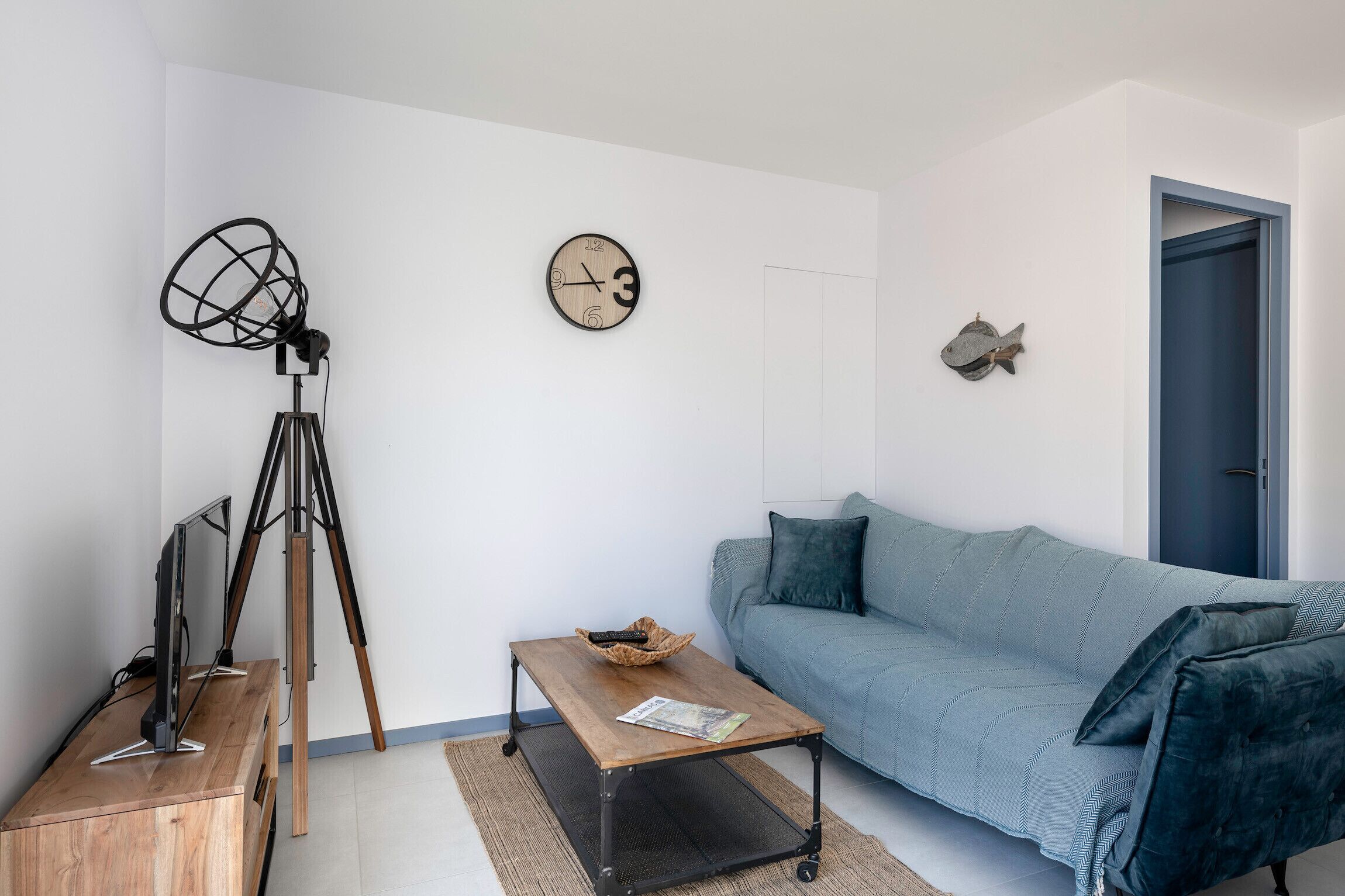 Un salon moderne avec une table basse en bois, un canapé bleu, une horloge murale et un trépied.