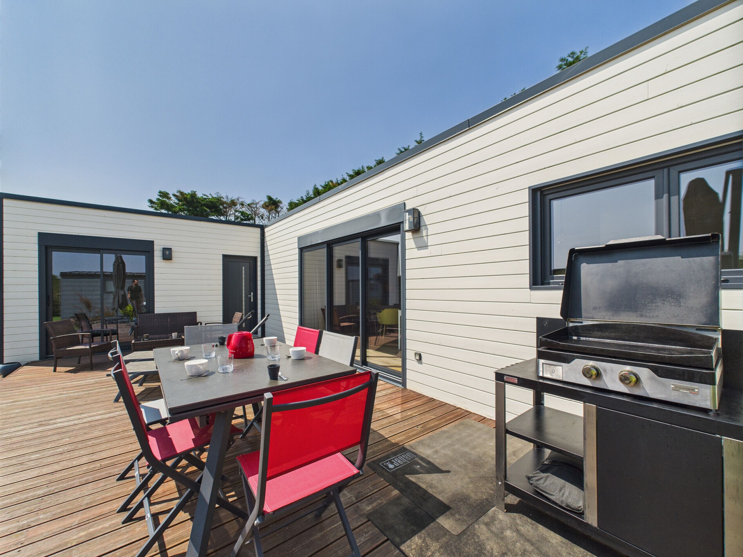 A modern outdoor patio with a dining table and chairs, a barbecue grill, and a deck.