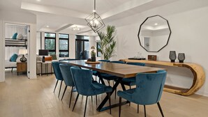A modern dining area with a long wooden table, blue velvet chairs, a geometric pendant light, and a large octagonal mirror. - Tremblant Prestige - Verbier 1-103 (Mont-Tremblant)