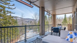 A covered outdoor patio with a view of a snowy landscape, a table with chairs, and a sofa with a pineapple-patterned pillow. - Tremblant Prestige - Verbier 1-103 (Mont-Tremblant)