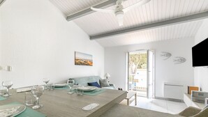 Un comedor moderno con una mesa de madera dispuesta para una comida, un sofá con cojines y vistas al exterior a través de un ventanal.