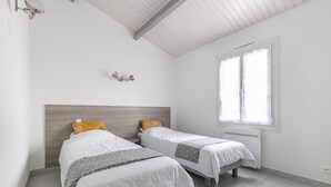 Un dormitorio con dos camas, cabeceros de madera, una ventana con persianas y una lámpara fijada a la pared.