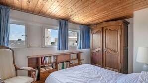 A bedroom with a wooden ceiling, a large bed, a wooden wardrobe, a chair, a bookshelf, and a window with curtains. - Superb sea view - Holidays for 5 people in Arzon (Arzon)