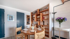 A dining area with a round wooden table, four wicker chairs, and a bookshelf filled with books and decorative items. - Superb sea view - Holidays for 5 people in Arzon (Arzon)