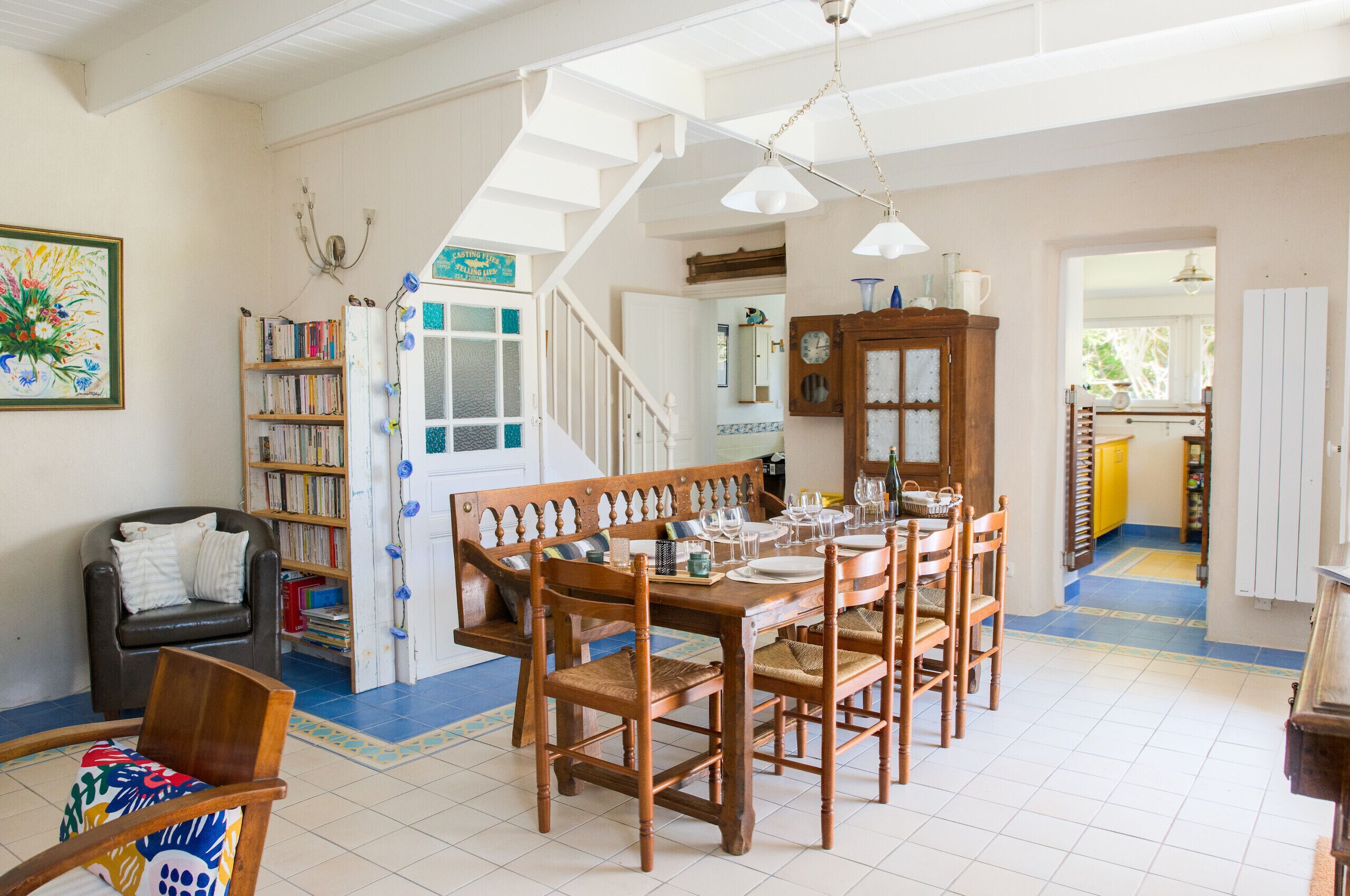 A dining area with a wooden table and chairs, a bookshelf, and a staircase leading to another room.