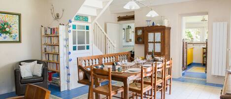 A dining area with a wooden table and chairs, a bookshelf, and a staircase leading to another room.