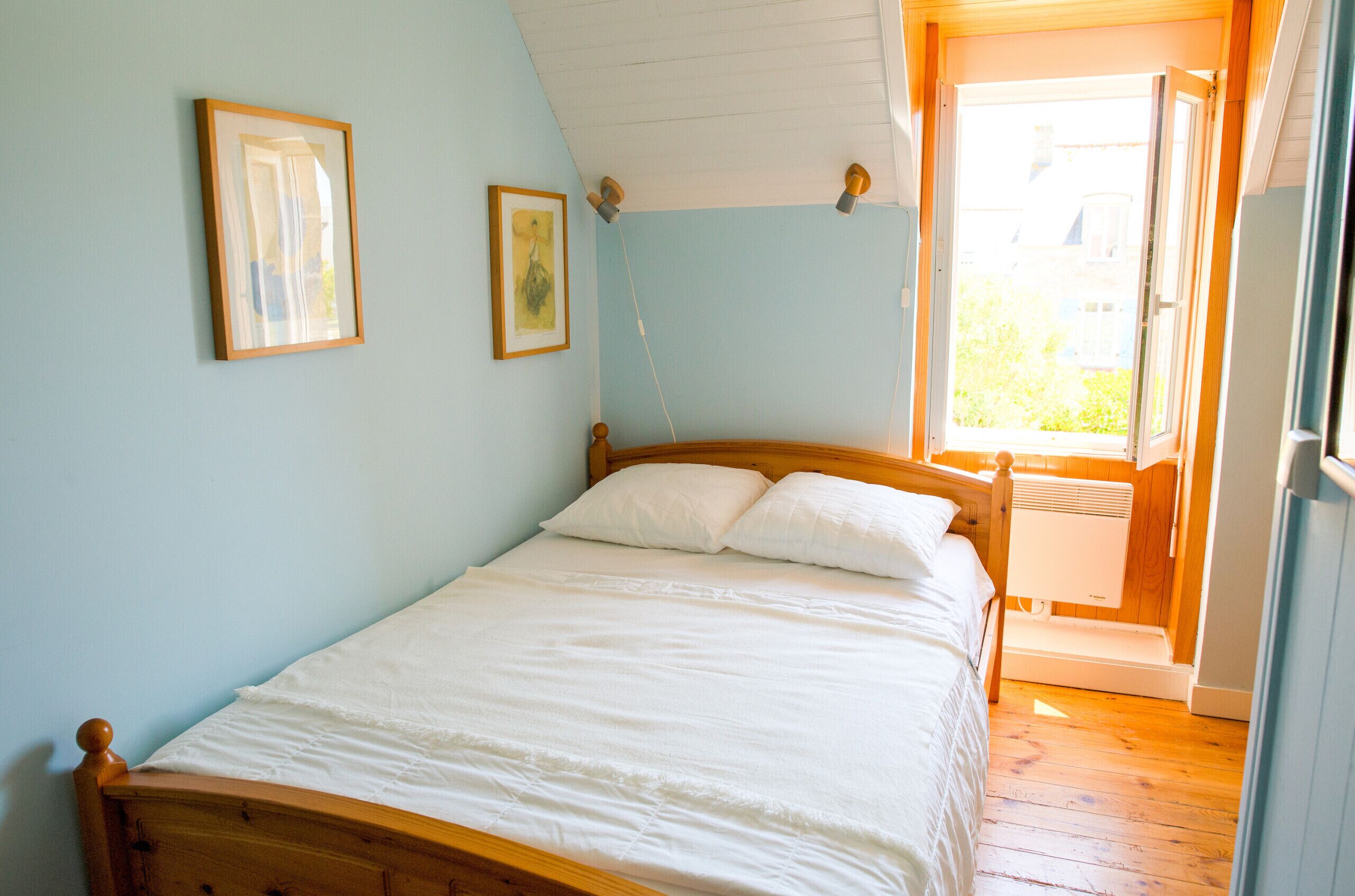 Une chambre à coucher avec un lit en bois, des murs bleu clair et une fenêtre donnant sur un paysage verdoyant.