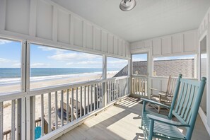 A covered porch with a view of the beach, wooden chairs, and a railing. - Thompson Up (Duplex - upstairs unit only), Oceanfront (Pawleys Island)