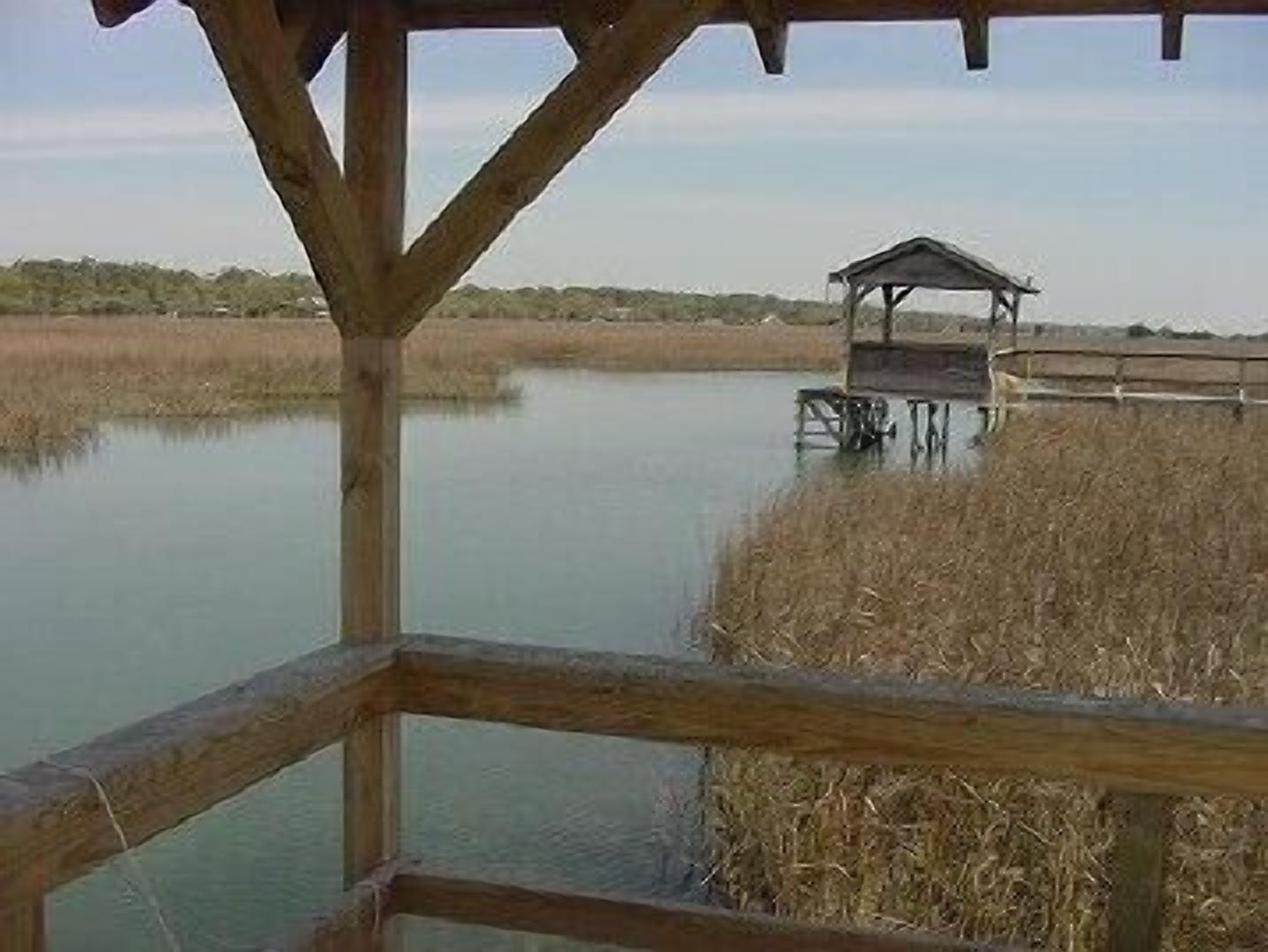 A wooden deck with a gazebo overlooking a calm body of water and marshland.
