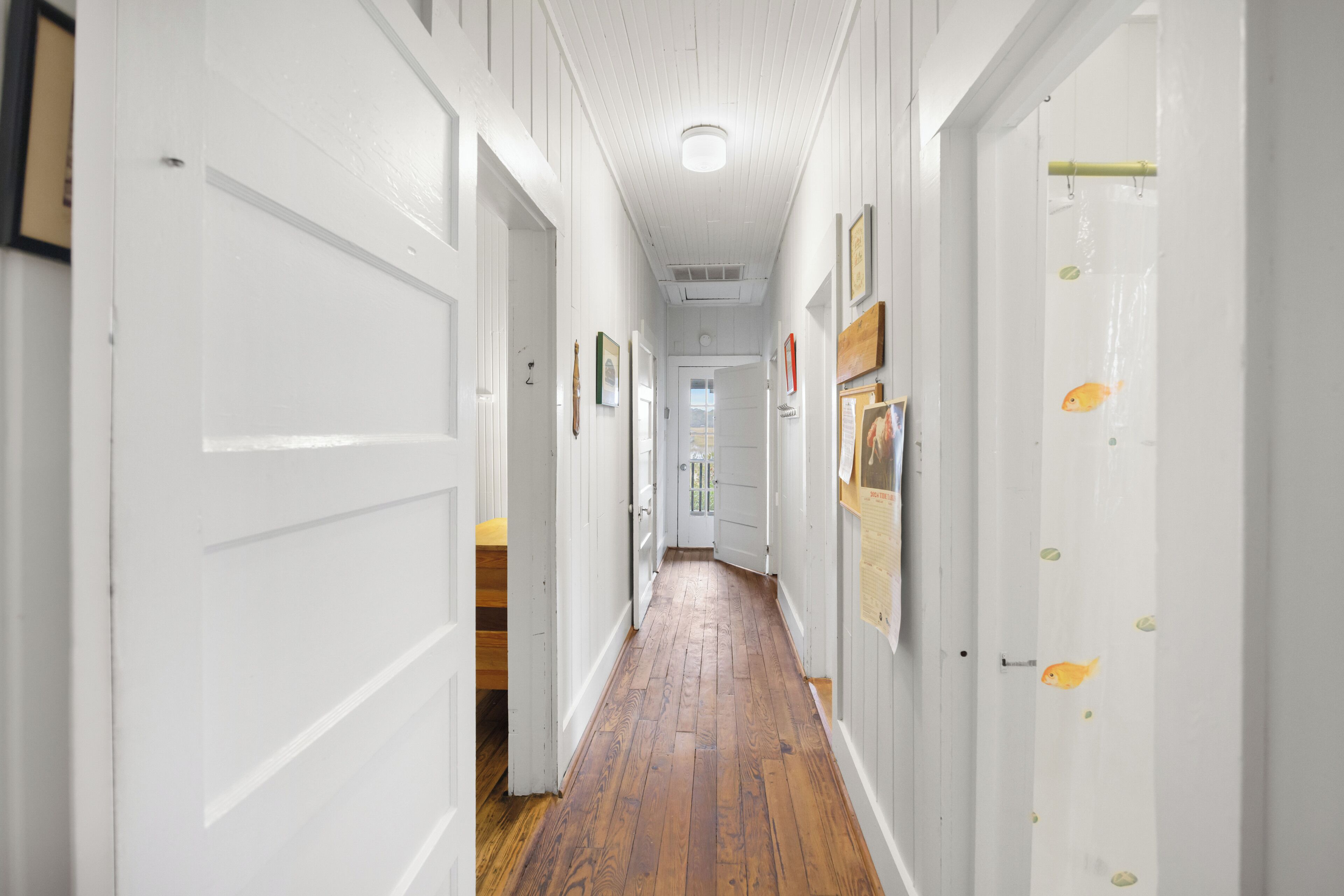 A narrow hallway with white walls and wooden floors, leading to a door at the end.