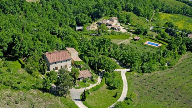 An aerial view of a rural property with a stone house, a swimming pool, and a winding path.