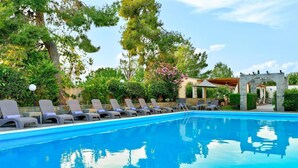 Una piscina con sillones de descanso y un arco de piedra.
