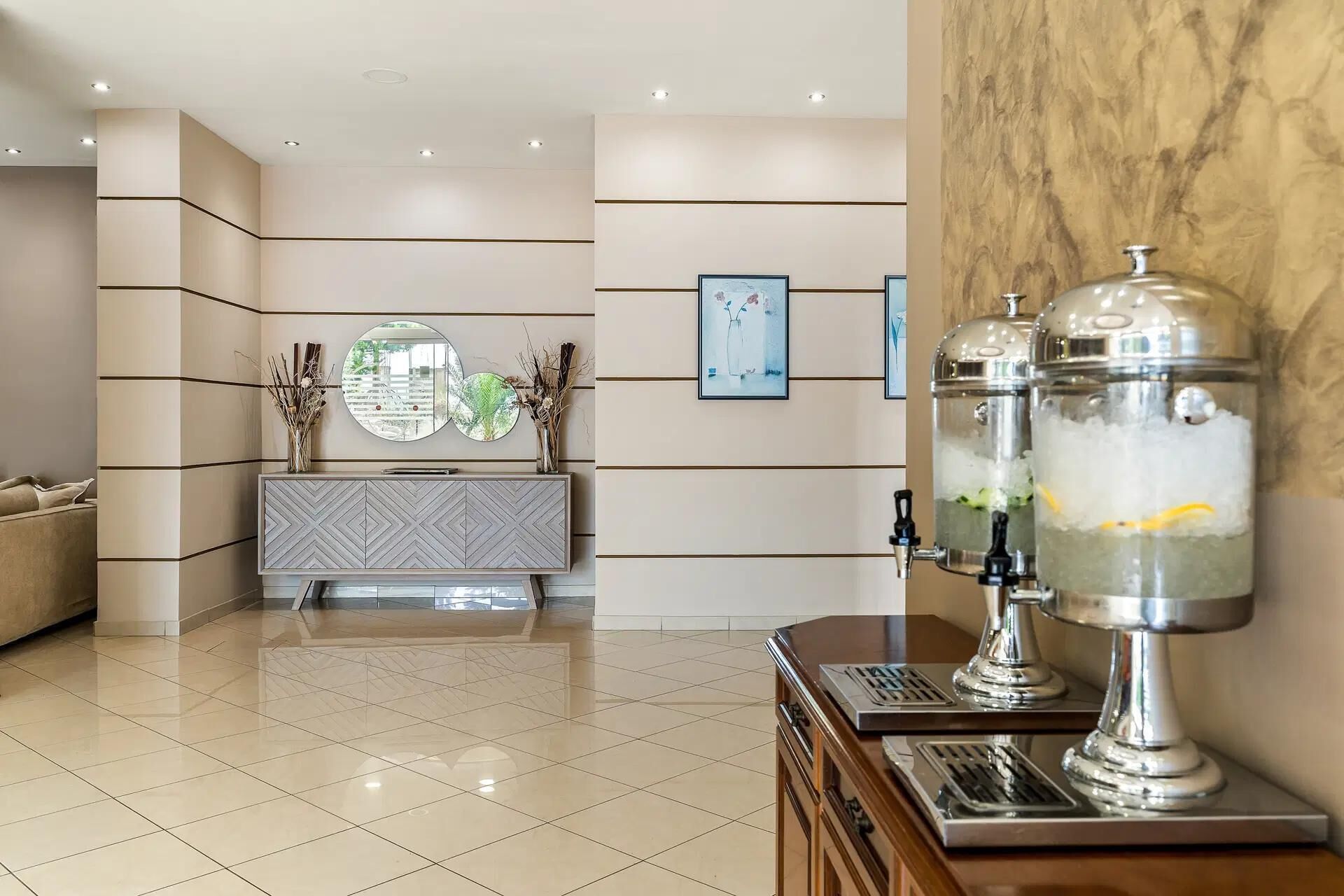 A hotel lobby with a modern design, featuring a marble reception desk, a mirrored wall, and a water dispenser.