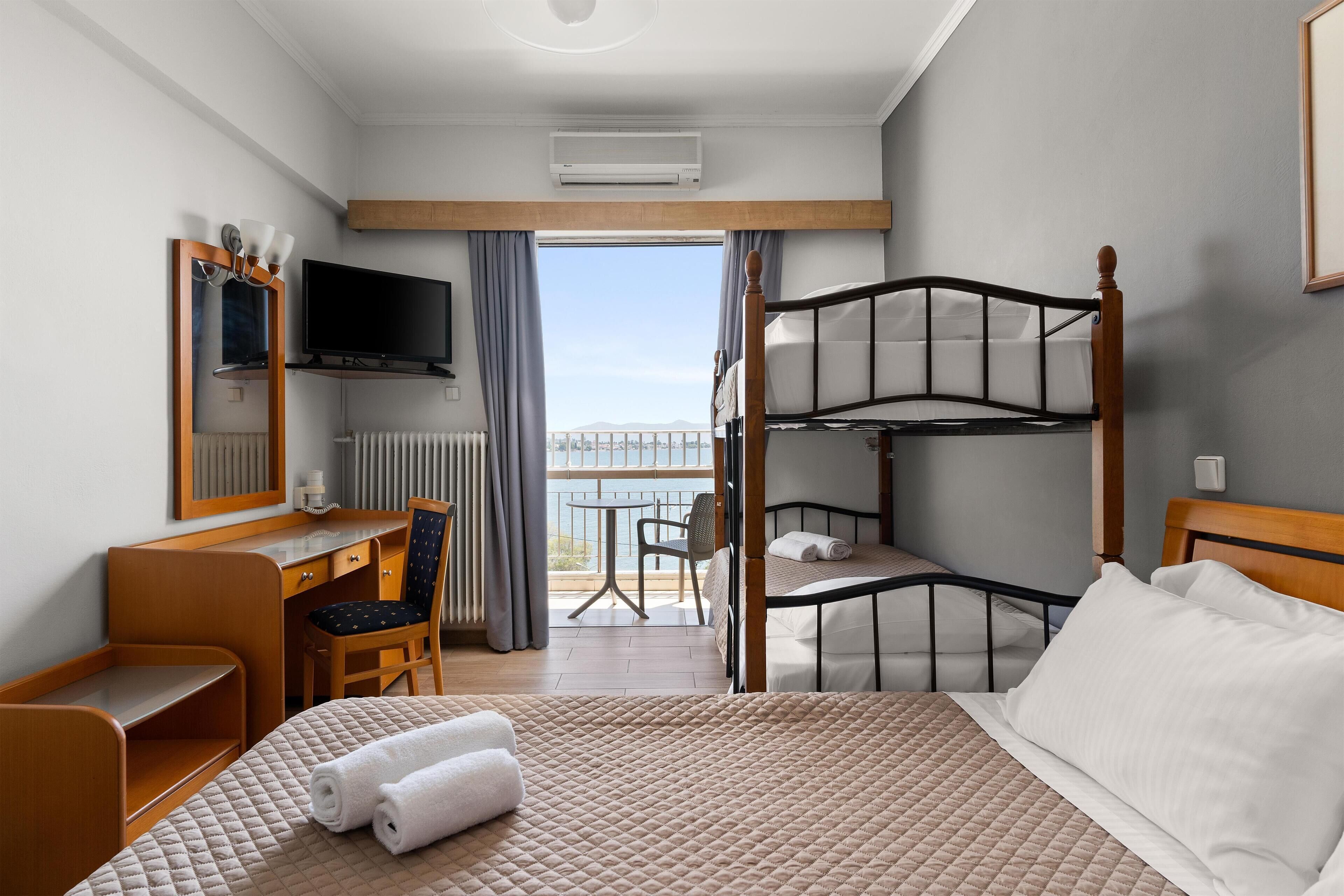 Una habitación de hotel con una cama litera, un escritorio con una silla, un televisor y vistas al balcón exterior.