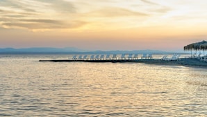 Una playa con sillas de descanso alineadas a lo largo de un muelle que se adentra en el agua.