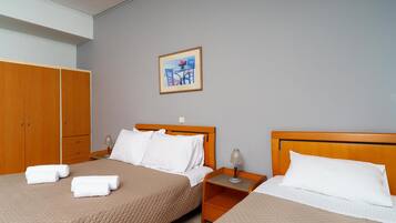 A hotel room with two beds, a wooden wardrobe, a nightstand with a lamp, and a framed picture on the wall.