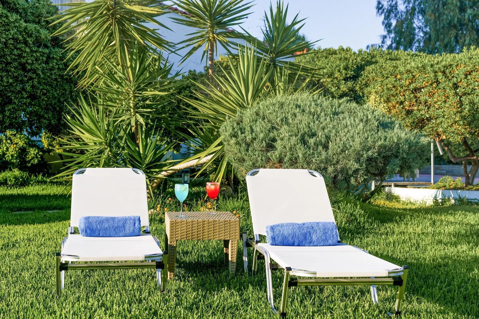 Twee lounge stoelen met blauwe handdoeken, een klein tafeltje met drankjes, en weelderige begroeiing op de achtergrond.
