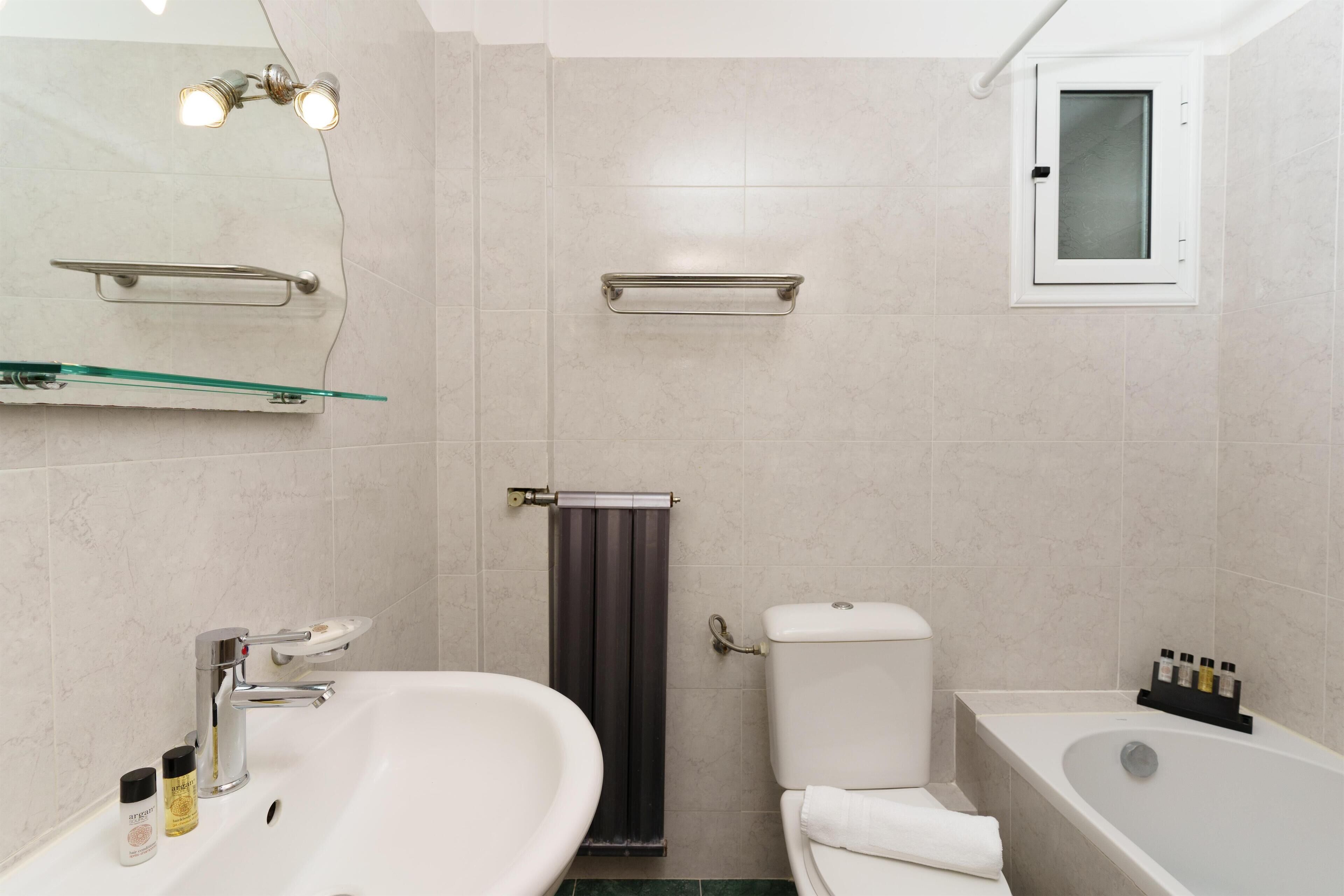 A bathroom with a white sink, a mirror, a glass shelf, a towel rack, a toilet, and a bathtub.
