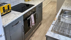 A modern kitchen with grey cabinets, a black stove, and a marble countertop. - New Day Properties-Seaside House-next to beach (South Shields)