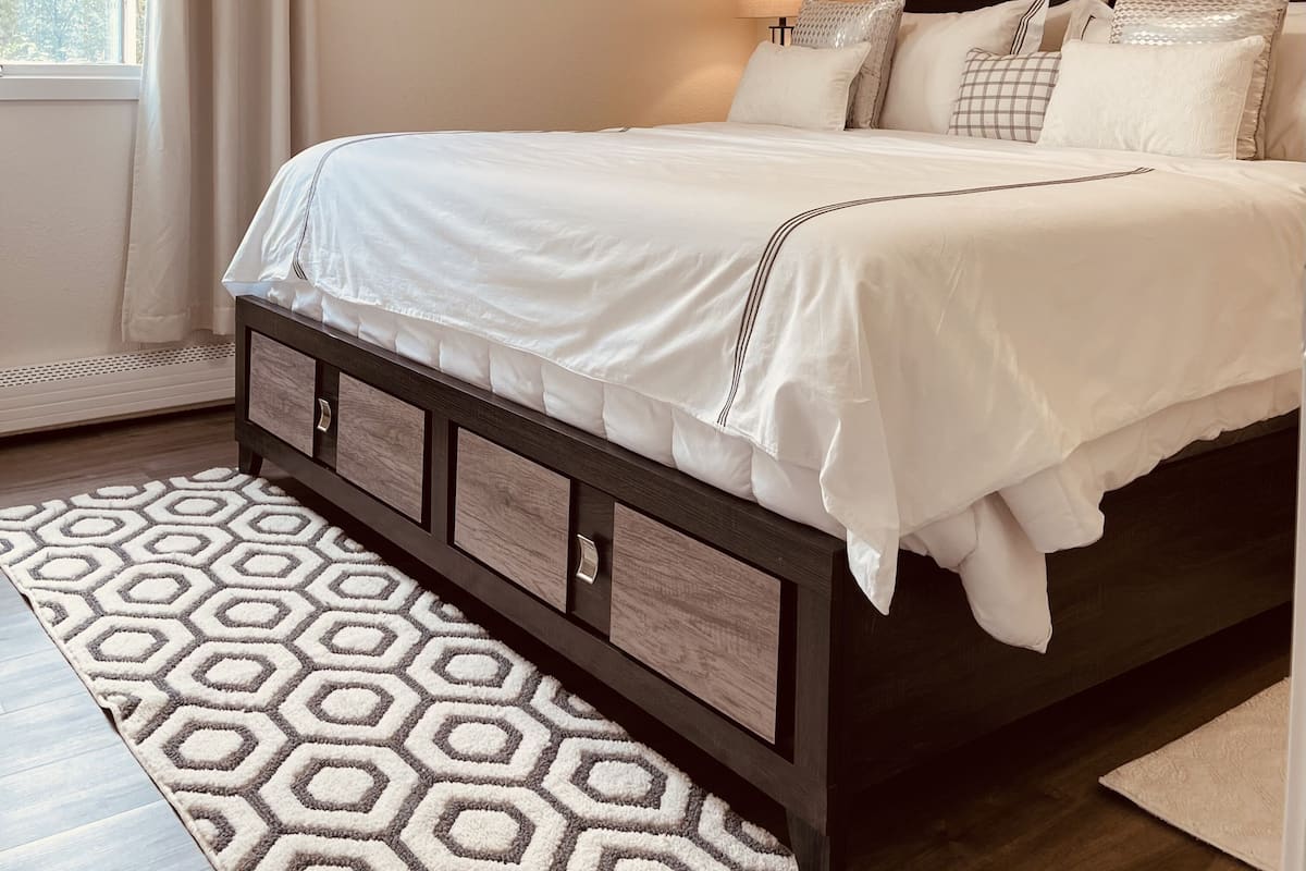 Una camera da letto ordinata con un letto, una lampada da comodino, un quadro appeso alla parete e un tappeto decorato.