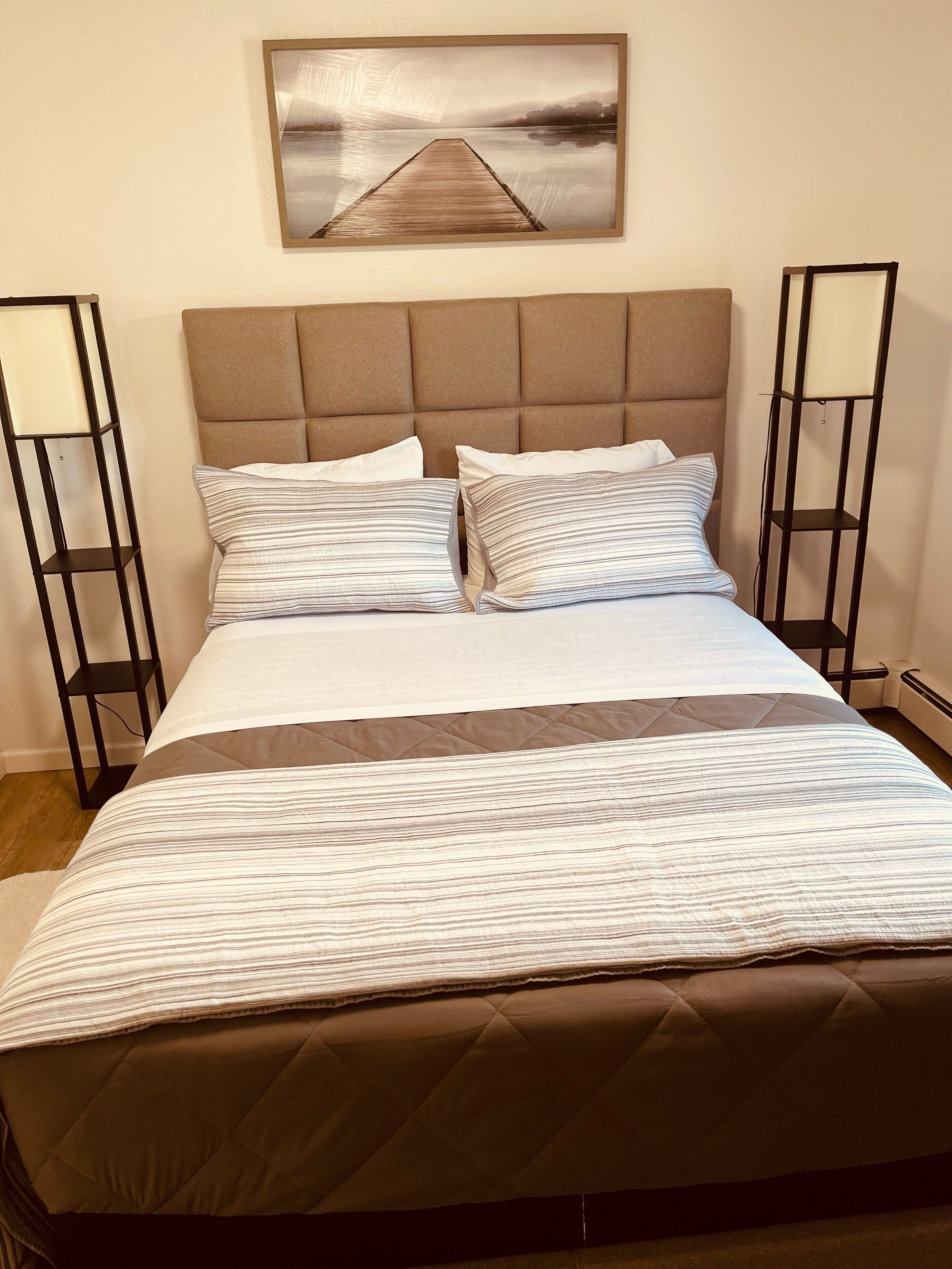 A neatly made bed with striped bedding, a headboard, and two bedside tables with lamps.