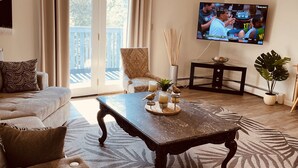 Ett vardagsrum med en stor TV, en soffa, ett soffbord och utsikt över omgivningarna.