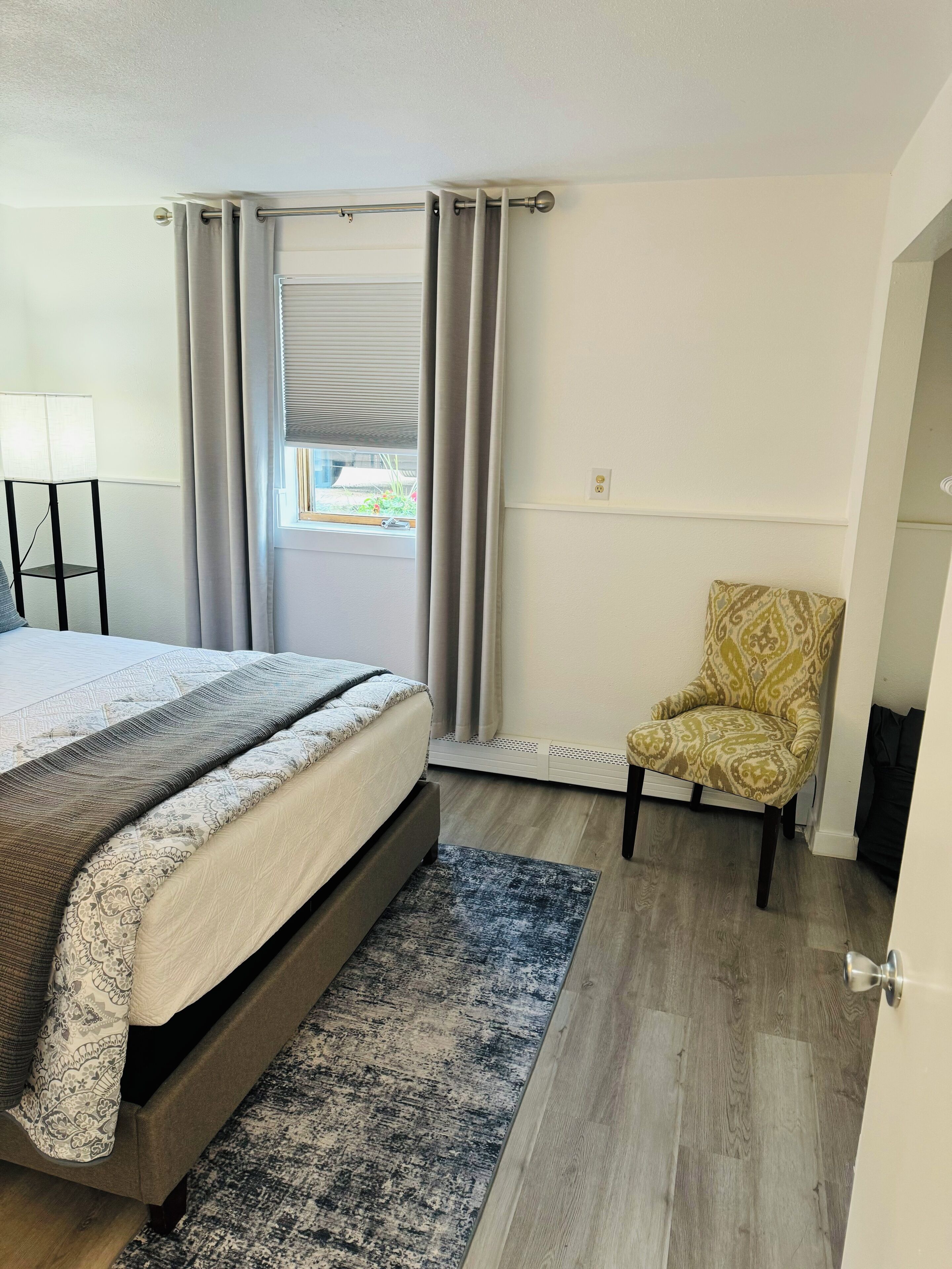 A bedroom with a bed, a chair, a floor lamp, and a window with curtains.