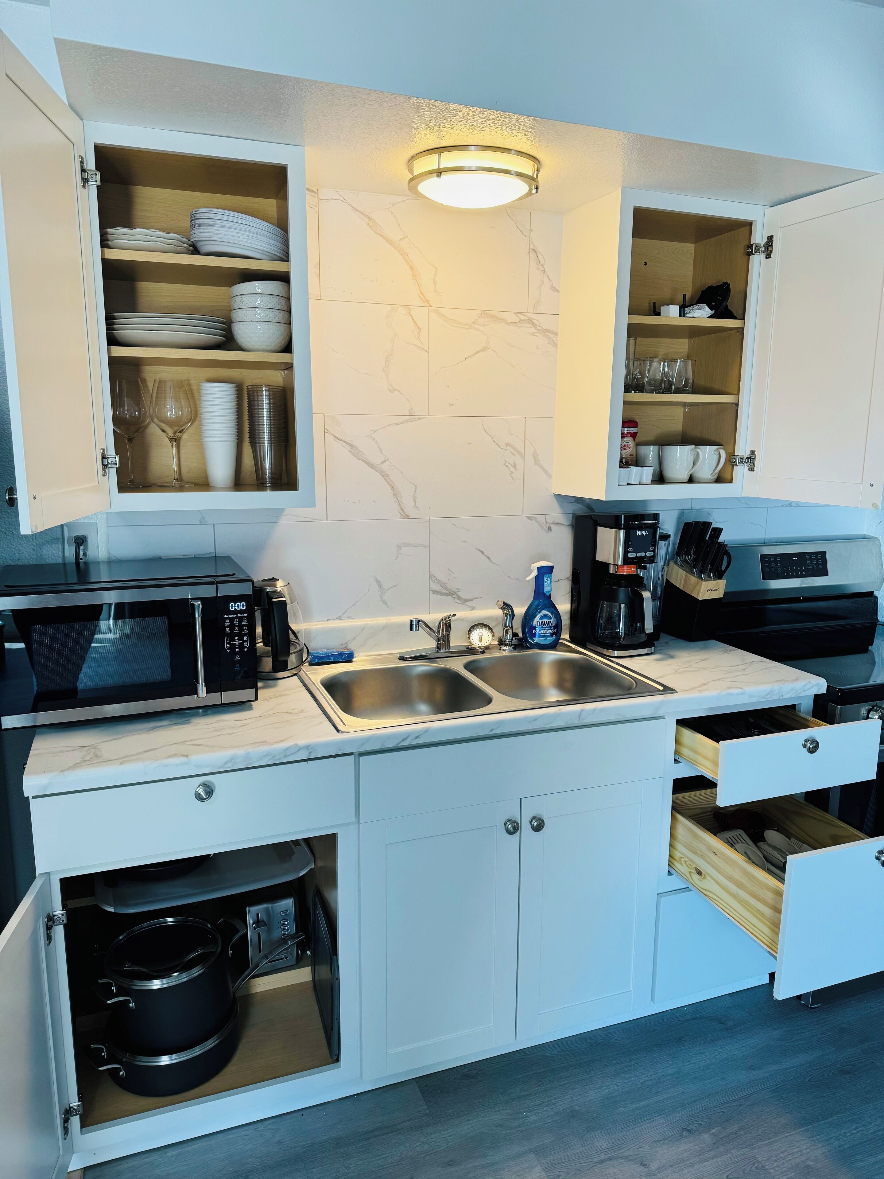 A modern kitchen with white cabinets, a built-in microwave, a double sink, and a coffee maker.