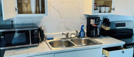 A modern kitchen with white cabinets, a built-in microwave, a double sink, and a coffee maker.