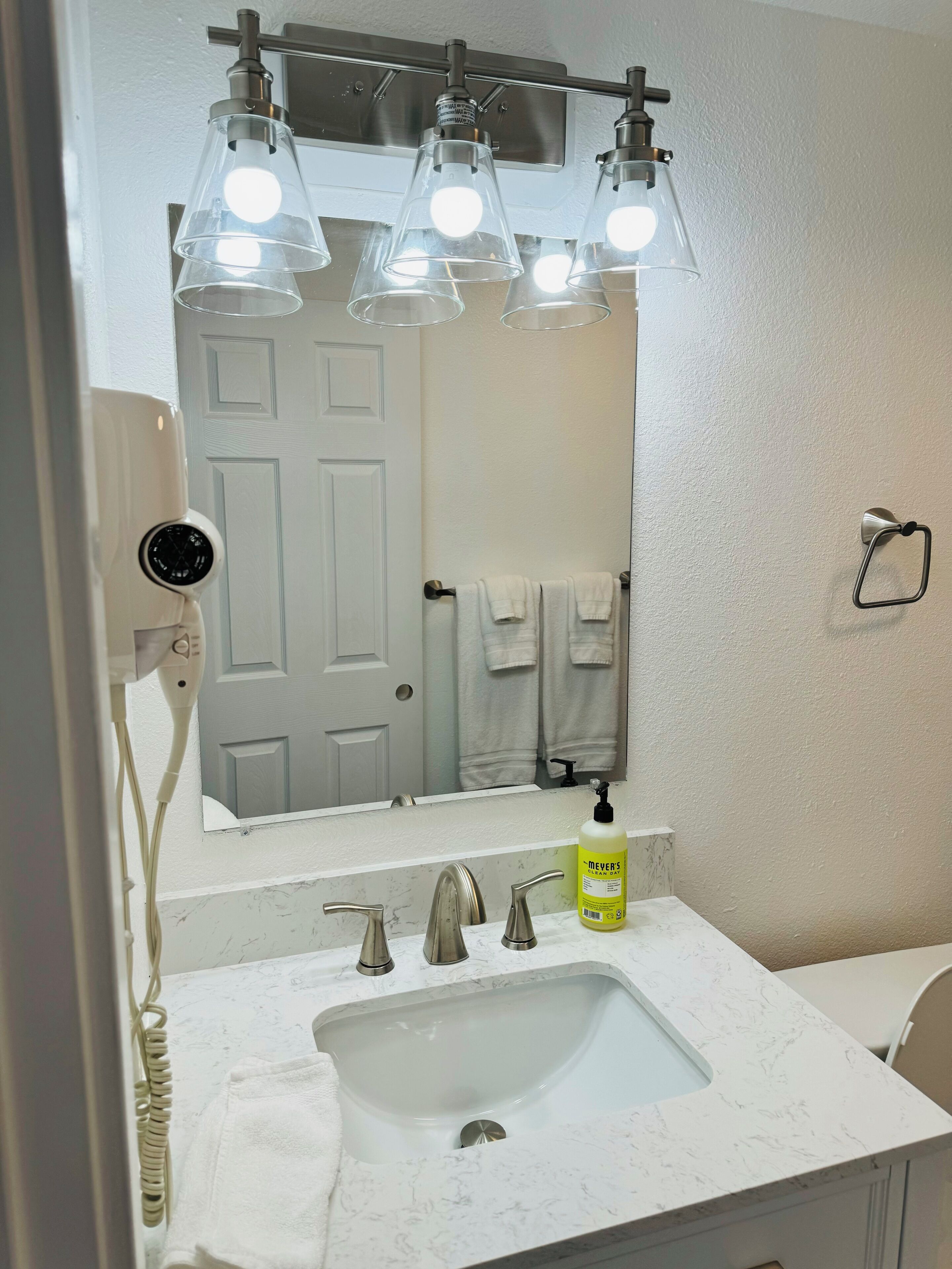 A bathroom with a white sink, three pendant lights, a towel rack with two towels, a hand dryer, and a bottle of hand soap.