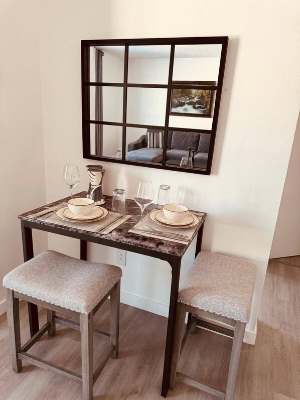 A dining area with a dark wooden table set for two, two matching chairs, and a large mirror above the table. - North Star Place (Fairbanks)